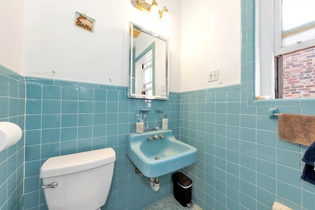 bathroom featuring a wainscoted wall, toilet, a sink, and tile walls