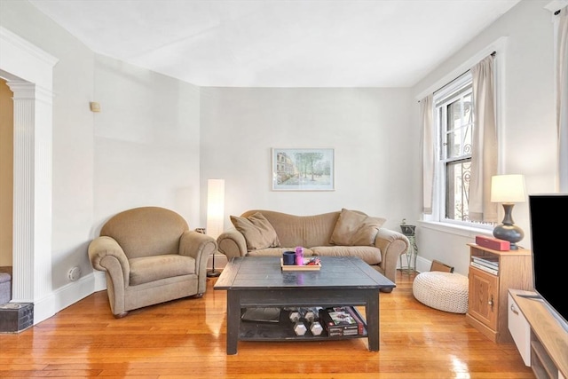 living room with light wood-style floors, baseboards, and ornate columns