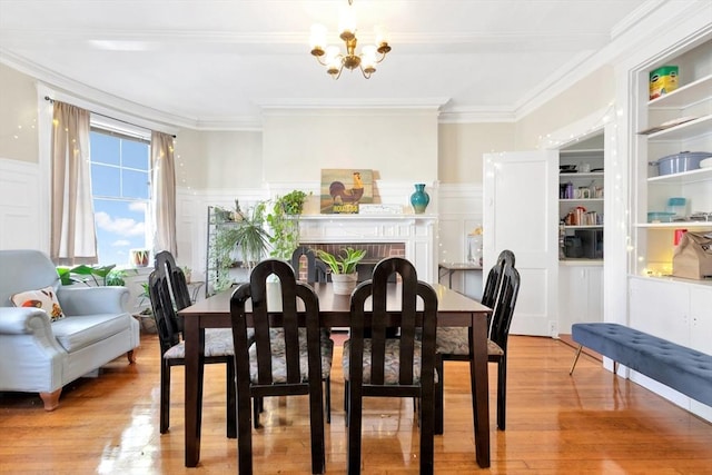 dining room featuring crown molding, wood finished floors, a chandelier, wainscoting, and a decorative wall