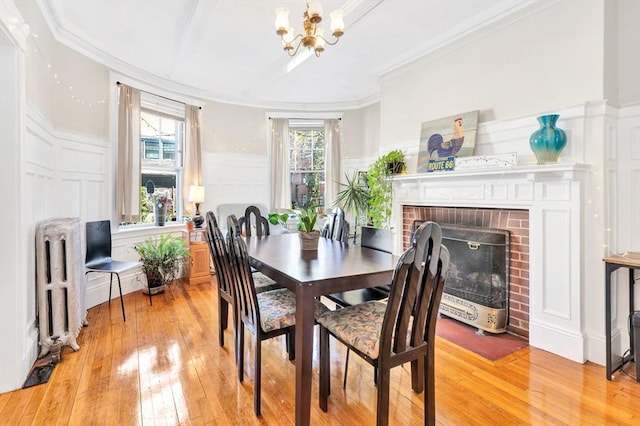 dining area featuring a decorative wall, light wood finished floors, a chandelier, crown molding, and radiator