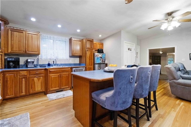 kitchen featuring ceiling fan, a center island, stainless steel fridge, light hardwood / wood-style flooring, and a kitchen bar