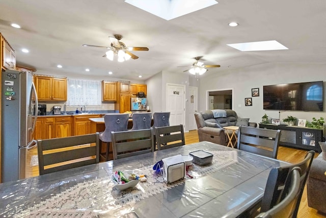 dining area featuring ceiling fan, sink, light wood-type flooring, and lofted ceiling with skylight