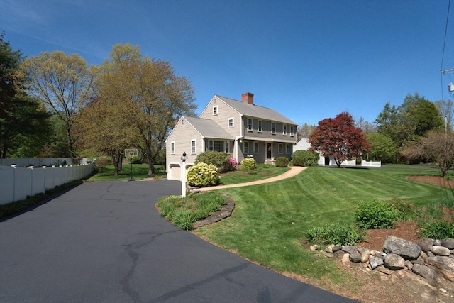 view of side of home featuring fence, aphalt driveway, a garage, a chimney, and a lawn