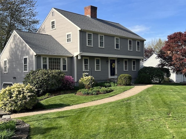 colonial-style house featuring a shingled roof, a front lawn, and a chimney