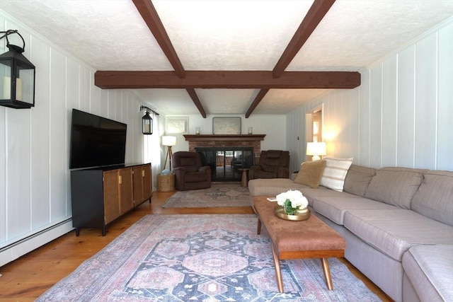 living area featuring baseboard heating, a fireplace, beam ceiling, light wood-style floors, and a decorative wall
