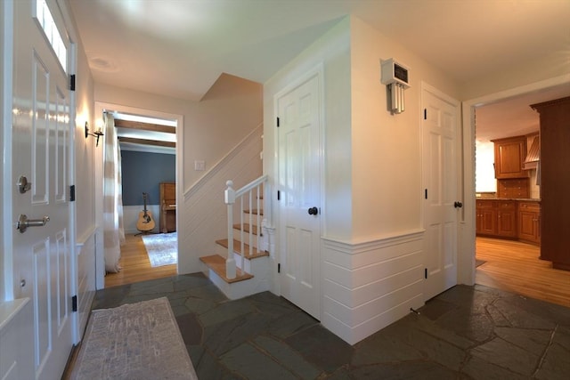 hallway with stone finish floor, stairway, and a wainscoted wall