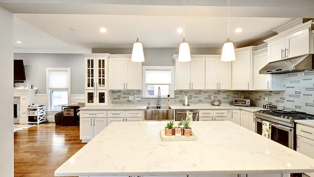 kitchen with appliances with stainless steel finishes, light stone countertops, a kitchen island, pendant lighting, and dark hardwood / wood-style flooring