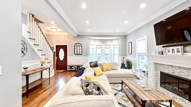 living room with a tiled fireplace, wood-type flooring, and crown molding