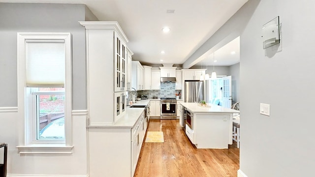 kitchen featuring stainless steel appliances, light wood-type flooring, a center island, white cabinets, and pendant lighting