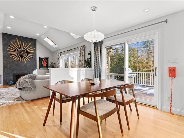 dining area featuring a large fireplace, lofted ceiling with skylight, and light hardwood / wood-style floors