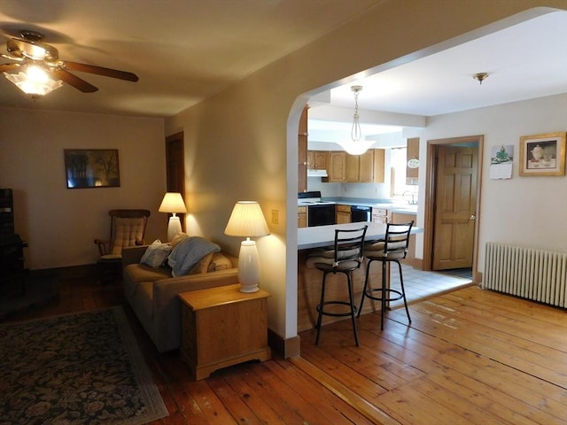 living area with radiator, arched walkways, wood-type flooring, and ceiling fan