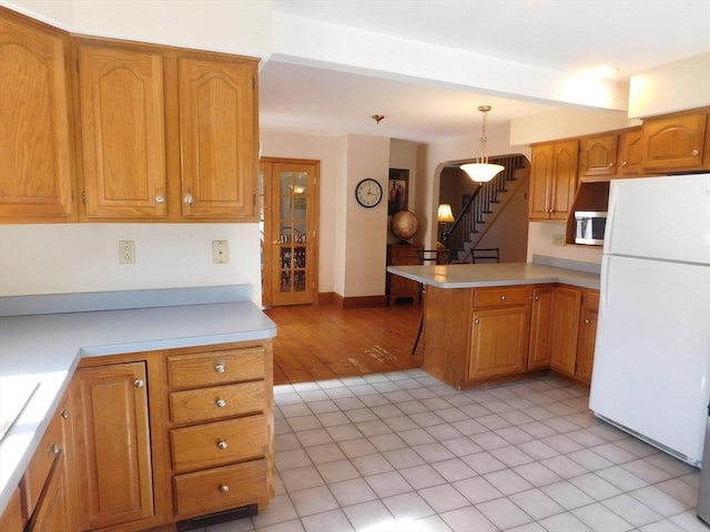 kitchen with stainless steel microwave, freestanding refrigerator, arched walkways, a peninsula, and light countertops