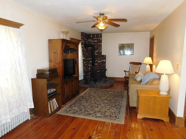 living area with baseboards, a ceiling fan, hardwood / wood-style floors, and a wood stove