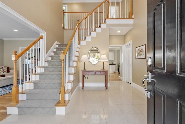 foyer with crown molding, light tile patterned floors, a high ceiling, baseboards, and stairs