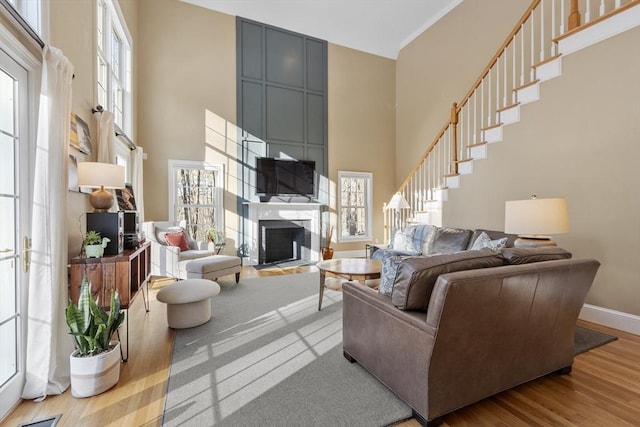 living area featuring a large fireplace, a high ceiling, baseboards, and wood finished floors