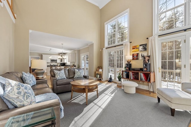 living area with a high ceiling, a chandelier, a wealth of natural light, and ornamental molding