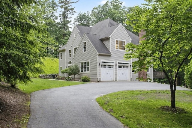 view of front facade with roof with shingles, a chimney, aphalt driveway, and a front yard