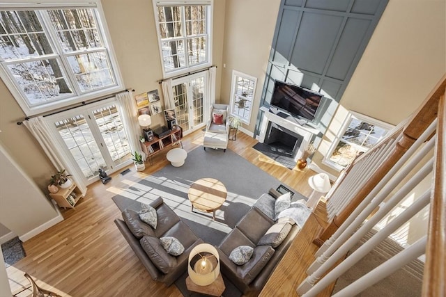 living room featuring french doors, a fireplace, a high ceiling, wood finished floors, and baseboards