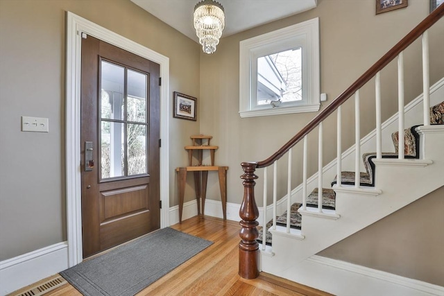 entryway with wood finished floors, visible vents, baseboards, stairway, and an inviting chandelier