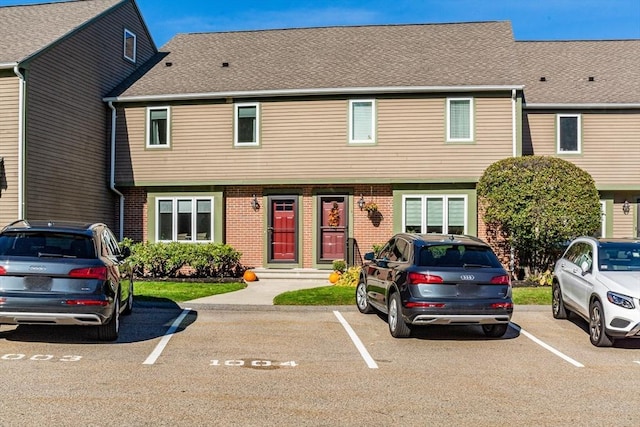 townhome / multi-family property featuring roof with shingles, uncovered parking, and brick siding