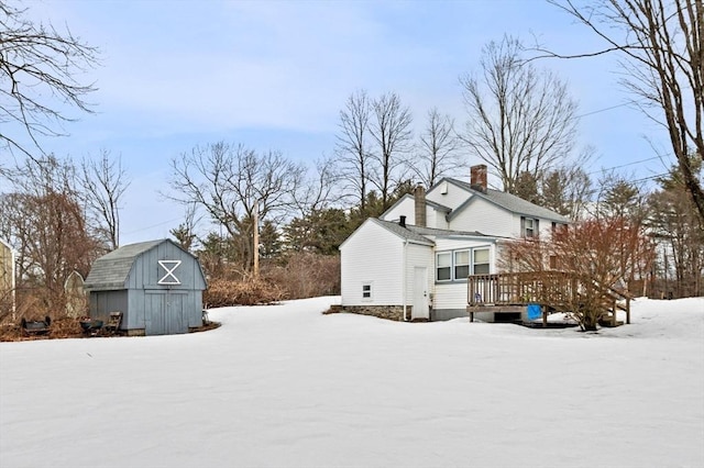 view of snow covered exterior featuring an outbuilding, a wooden deck, a storage unit, and a chimney