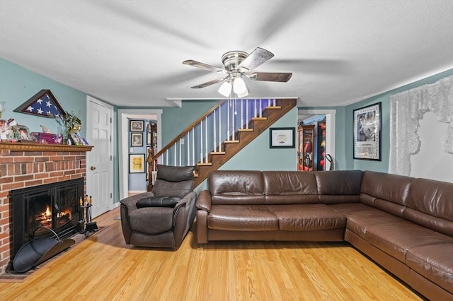 living room with a brick fireplace, stairs, ceiling fan, and wood finished floors