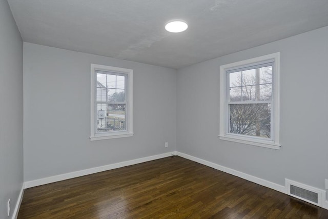 empty room with dark hardwood / wood-style flooring and a wealth of natural light