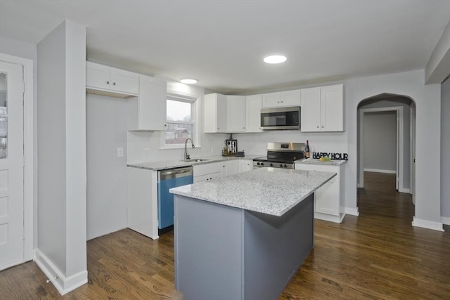 kitchen with light stone countertops, a center island, dark wood-type flooring, stainless steel appliances, and white cabinets