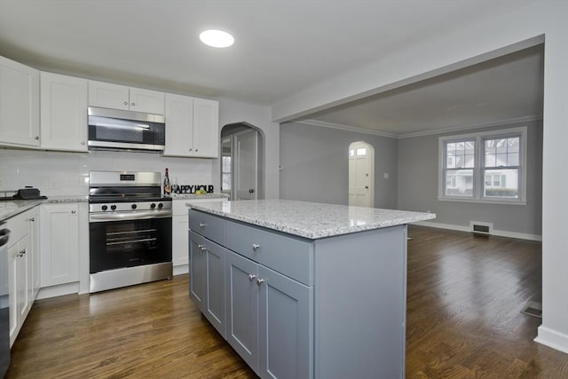 kitchen featuring white cabinets, tasteful backsplash, a kitchen island, light stone counters, and stainless steel appliances