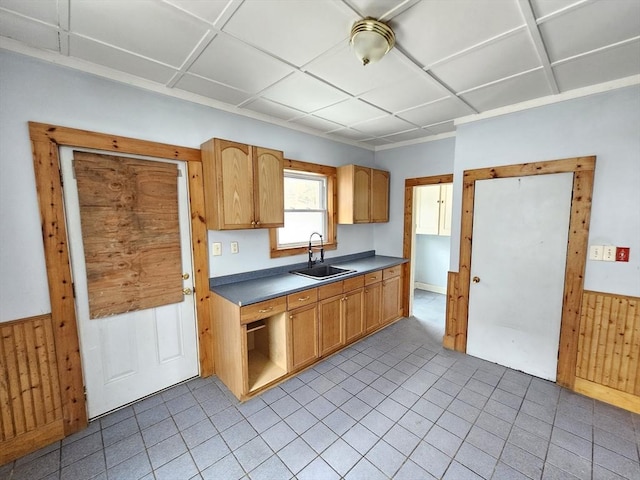 kitchen featuring wainscoting, a sink, wooden walls, and light tile patterned floors