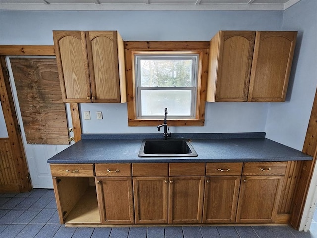 kitchen featuring dark countertops, brown cabinetry, tile patterned flooring, and a sink