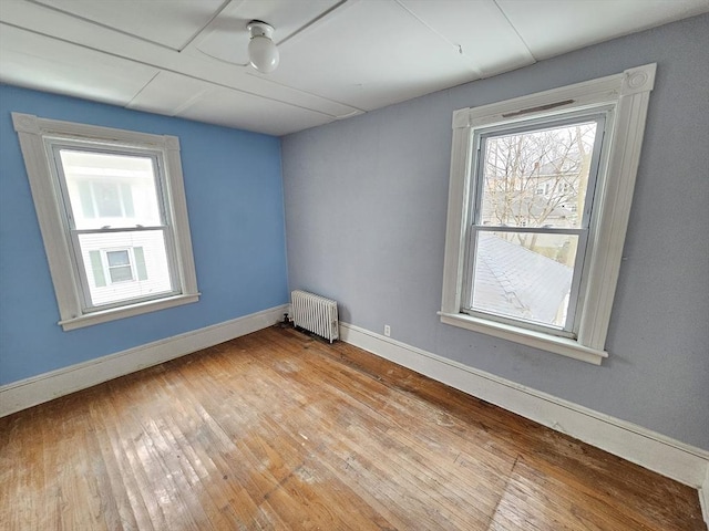 unfurnished room featuring baseboards, radiator heating unit, and light wood-style flooring