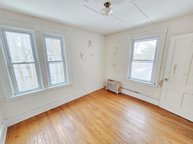 spare room with radiator heating unit, baseboards, and light wood-type flooring
