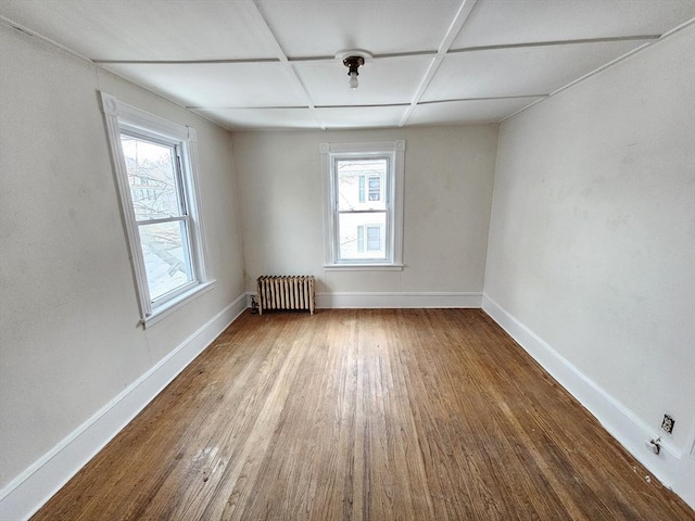 empty room featuring radiator, baseboards, wood finished floors, and plenty of natural light