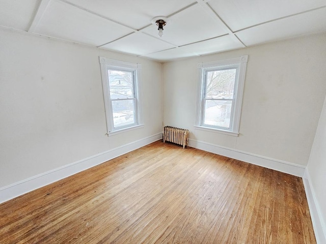 spare room featuring baseboards, radiator heating unit, light wood-type flooring, and plenty of natural light