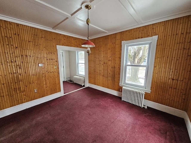spare room with crown molding, wood walls, dark carpet, and radiator