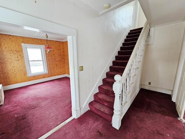 staircase with baseboards, crown molding, wooden walls, and carpet