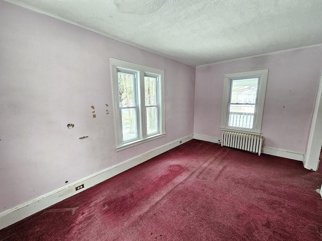 spare room with radiator, dark colored carpet, ornamental molding, baseboards, and a textured ceiling