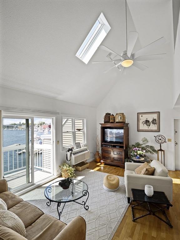 living room featuring a ceiling fan, lofted ceiling with skylight, an AC wall unit, and wood finished floors