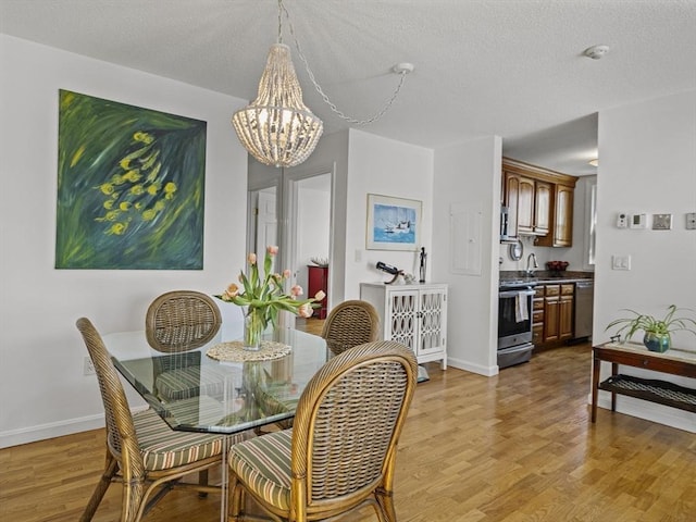 dining room with light wood finished floors, a textured ceiling, and a notable chandelier