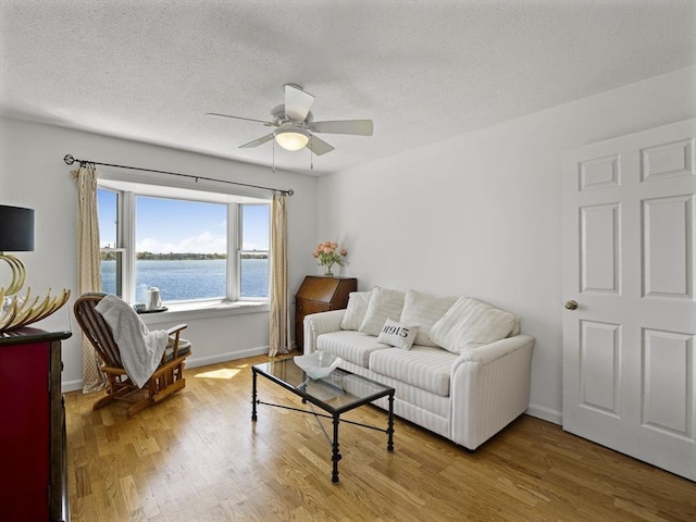 living room featuring a water view, wood finished floors, a textured ceiling, baseboards, and ceiling fan