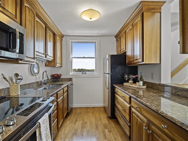 kitchen with a sink, dark stone countertops, light wood-style flooring, baseboards, and appliances with stainless steel finishes