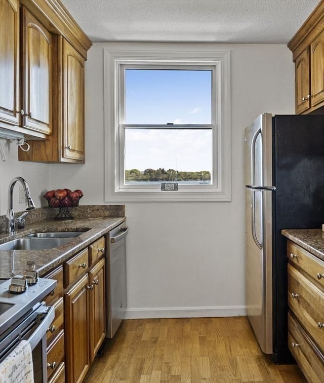 kitchen featuring a sink, brown cabinetry, light wood-type flooring, baseboards, and appliances with stainless steel finishes