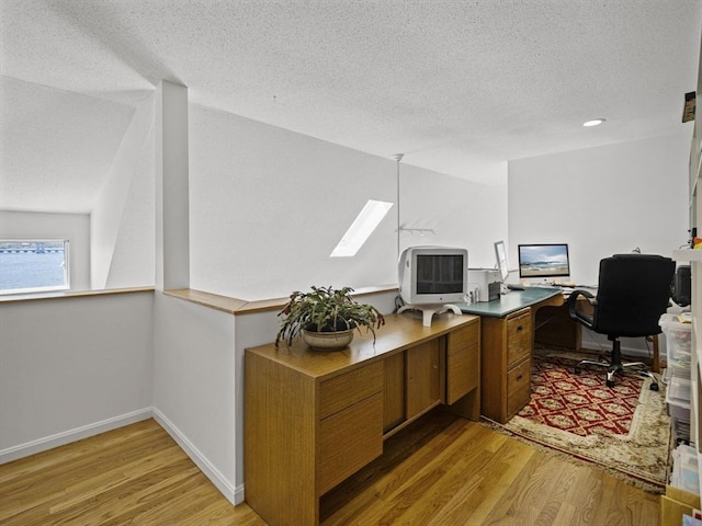 office with baseboards, a skylight, light wood-style flooring, and a textured ceiling