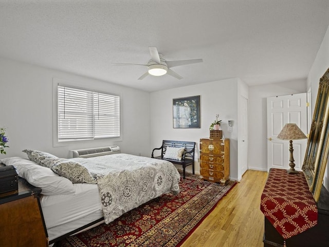 bedroom featuring a wall mounted air conditioner, light wood-type flooring, and ceiling fan