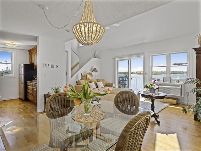dining area with a textured ceiling, light wood-style floors, baseboards, and a notable chandelier