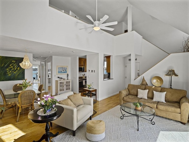 living area featuring baseboards, light wood-style floors, and ceiling fan with notable chandelier