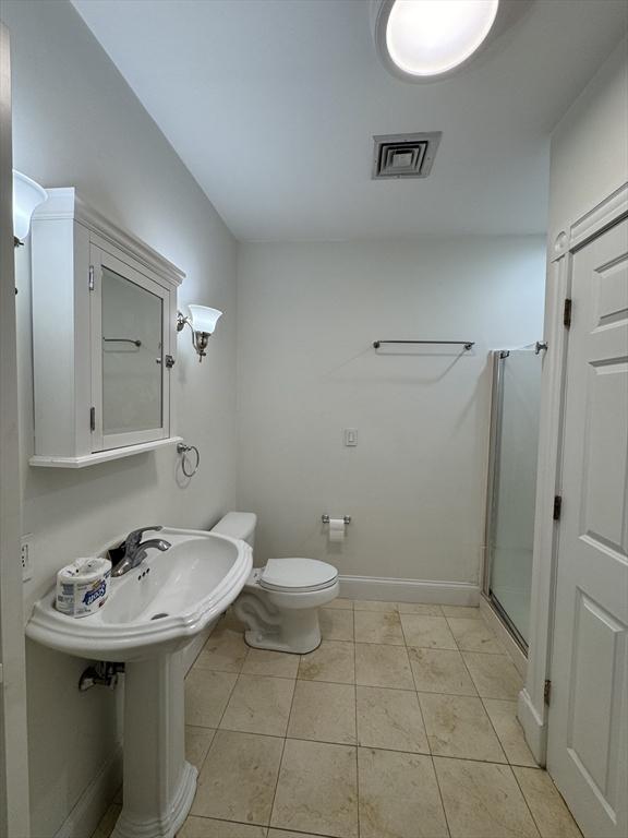 bathroom featuring tile patterned flooring, toilet, a shower with door, and sink