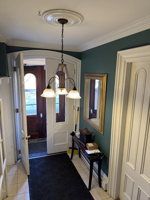 tiled entrance foyer featuring ornamental molding and an inviting chandelier