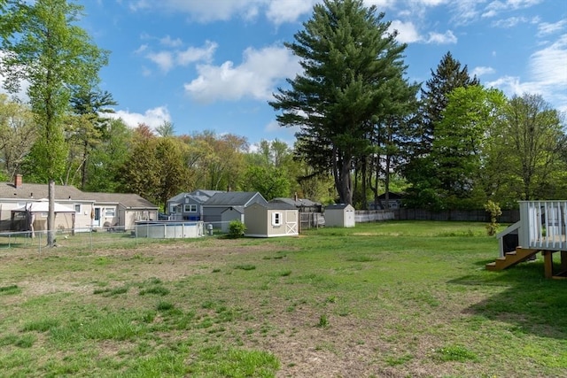 view of yard featuring a storage unit, an outdoor pool, an outbuilding, and view of wooded area